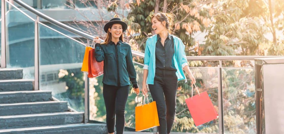 Two smiling women holding shopping bags walking down the stairs.