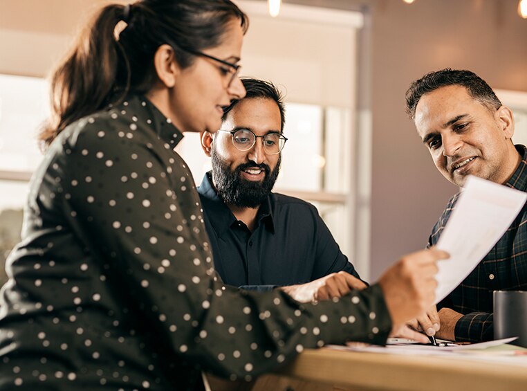 One woman and two men look down at a piece of paper. 