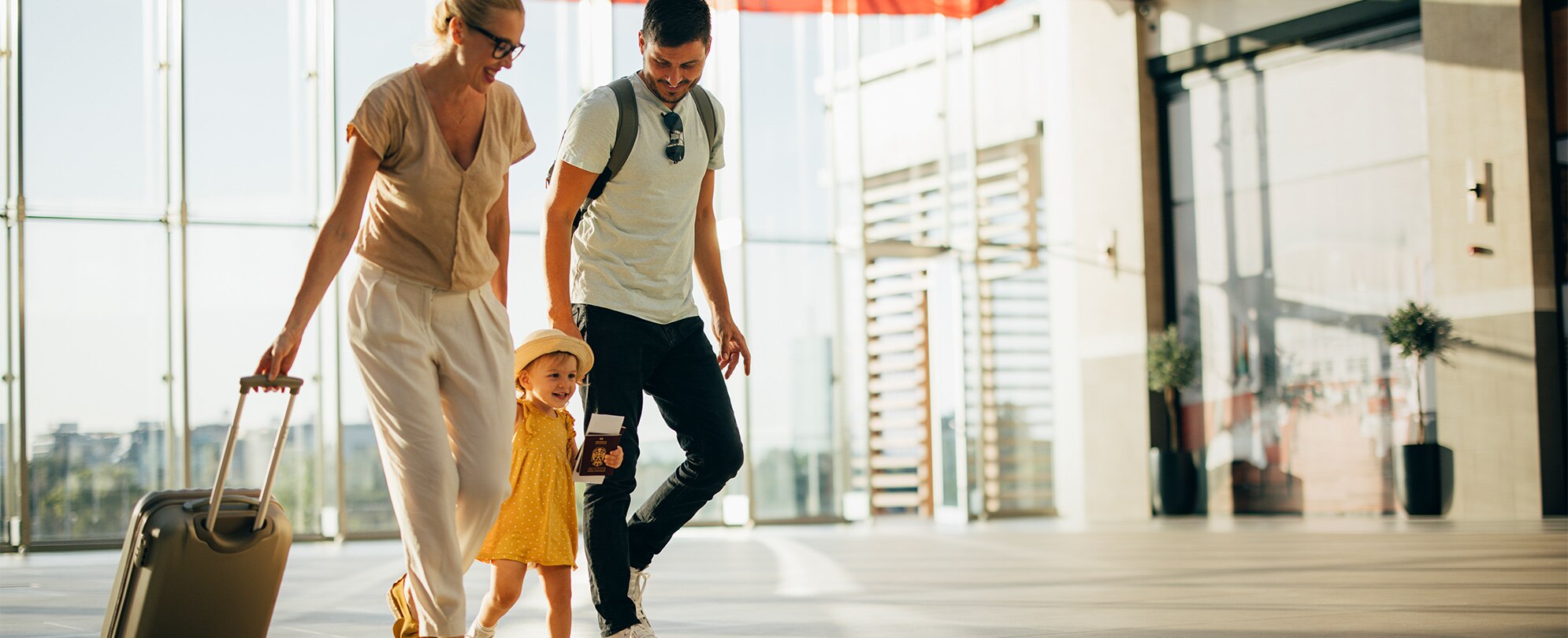 A family of three walking through the airport with their luggage.