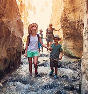 Two moms and two children holding hands while hiking down a stream, between canyons.