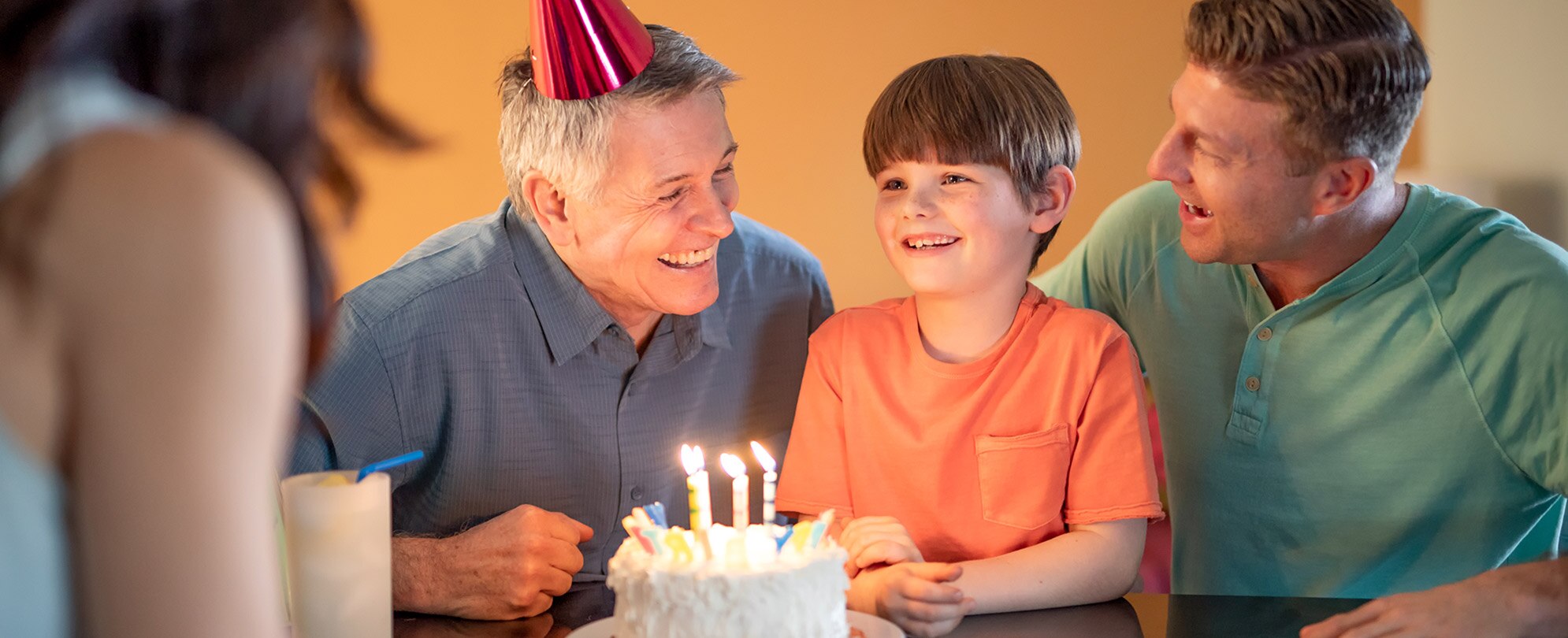 A young boy sits between two smiling fathers in front of a decorated birthday cake with candles.