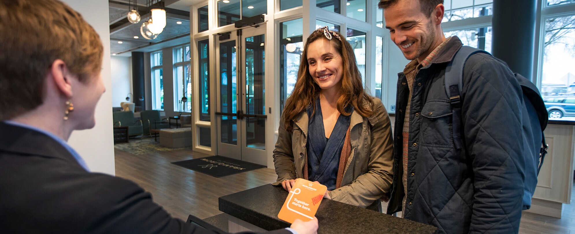 Smiling man and woman stand at the check-in counter across from a female WorldMark by Wyndham employee.