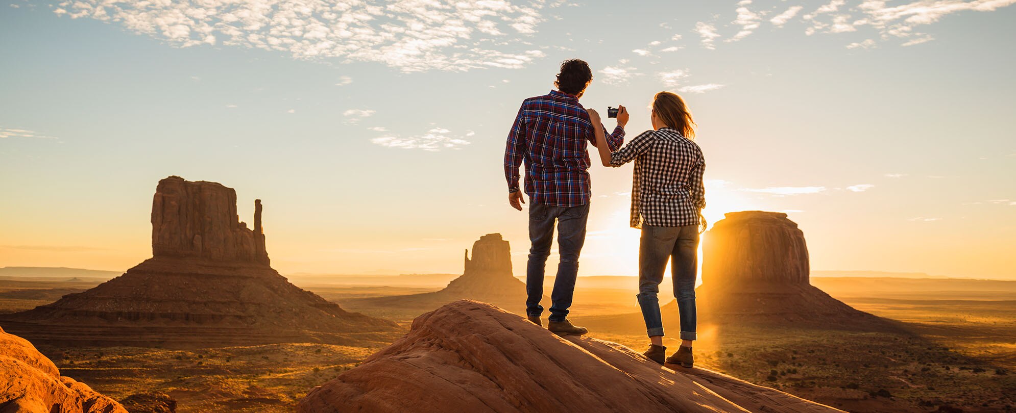 A man and woman standing on top of a rock ledge at sunset, looking out at rock formations in Moab, Utah.