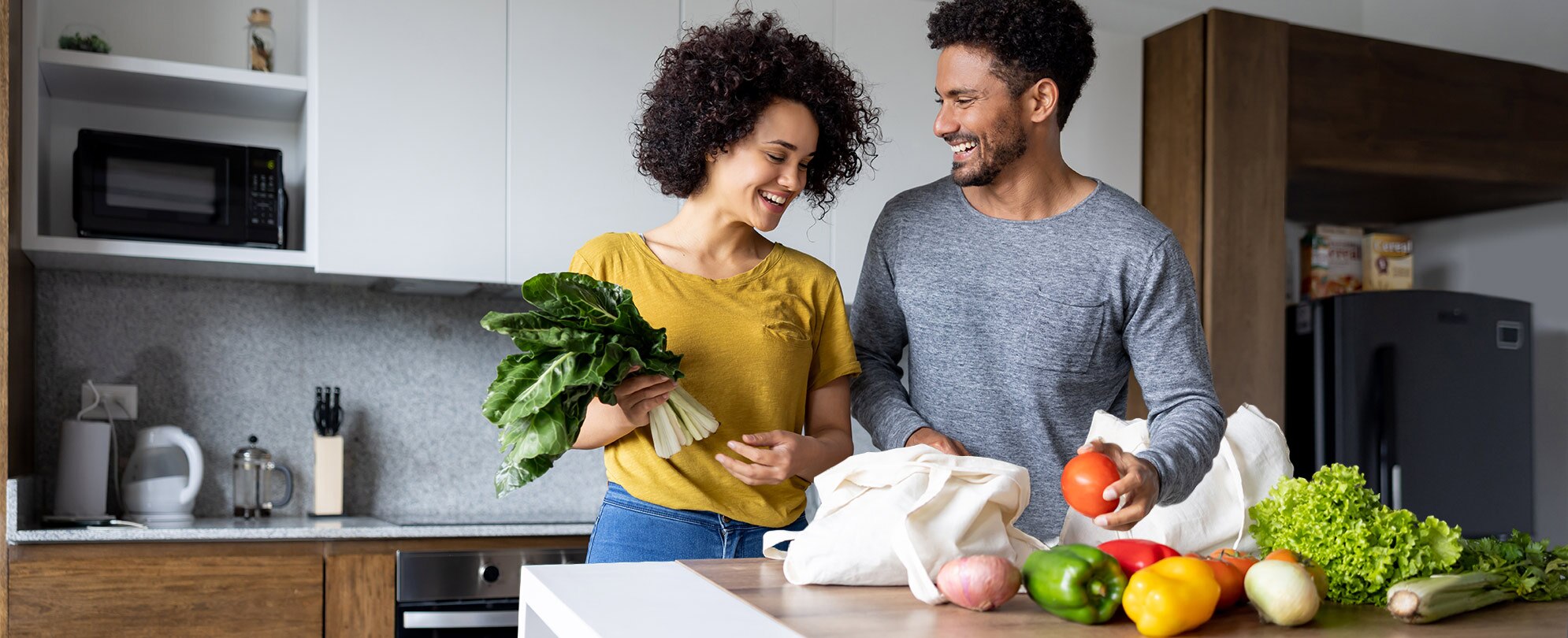 A couple in a kitchen are sorting their fresh produce on a counter.