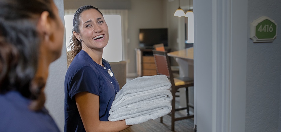 A smiling Club Wyndham employee holds a pile of towels as she enters a resort suite.